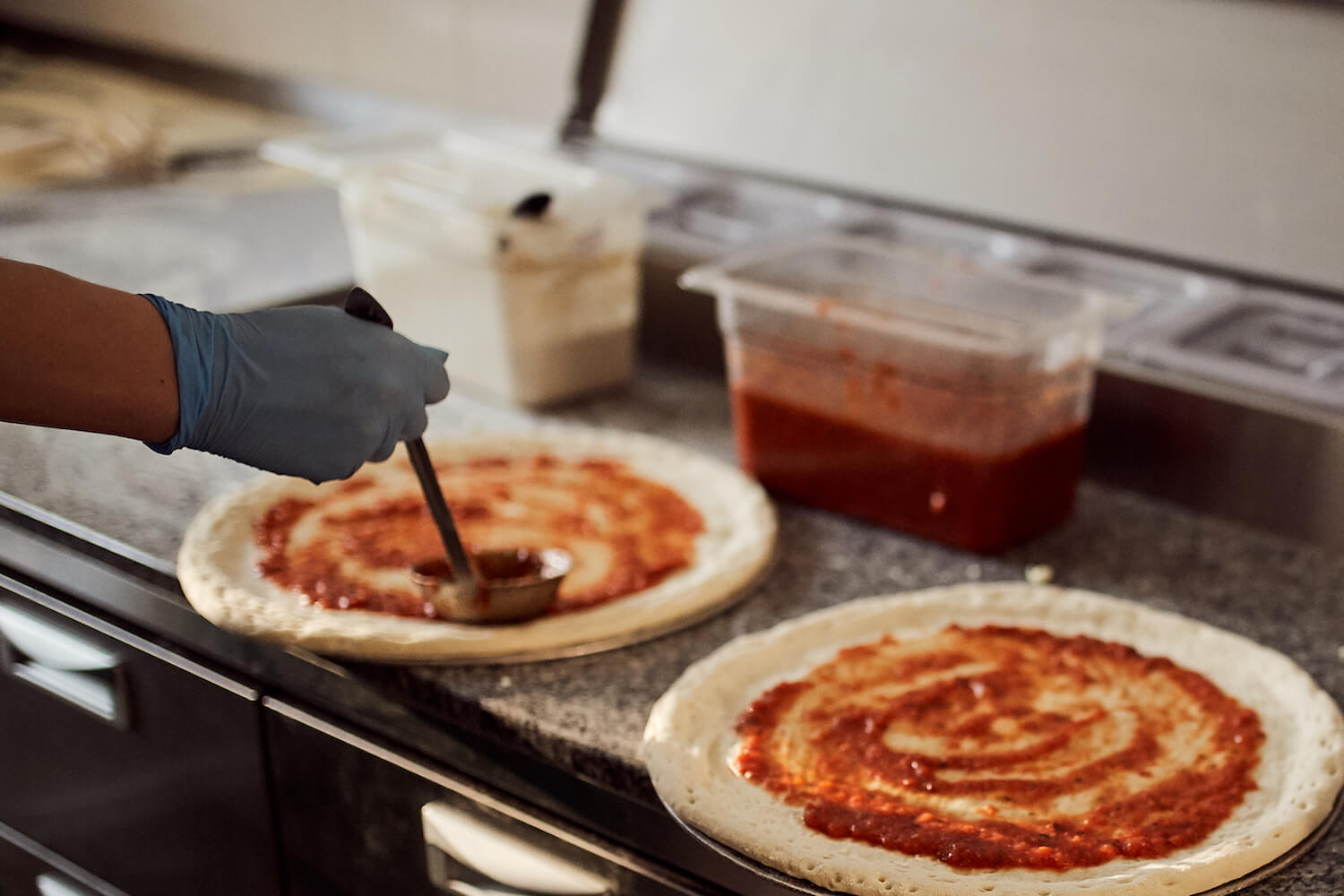Сотрудница пиццерии «О-пицца» размазывает томатный соус на тесто